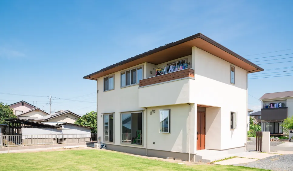 青空の下の白い2階建て住宅と芝生の庭